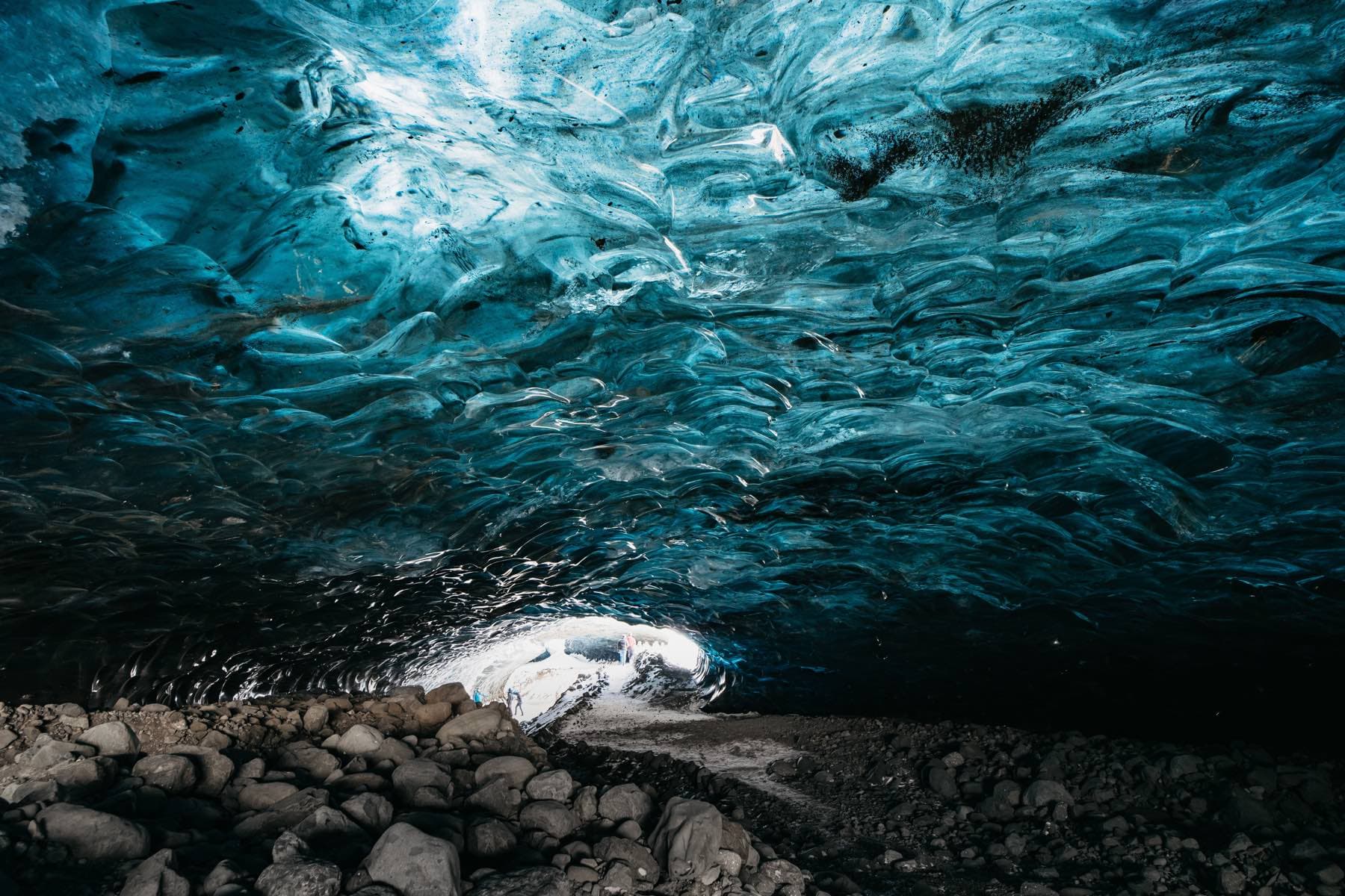 Inside a crystal-blue ice cave under Vatnajokull glacier, travellers silhouetted at the glowing entrance
