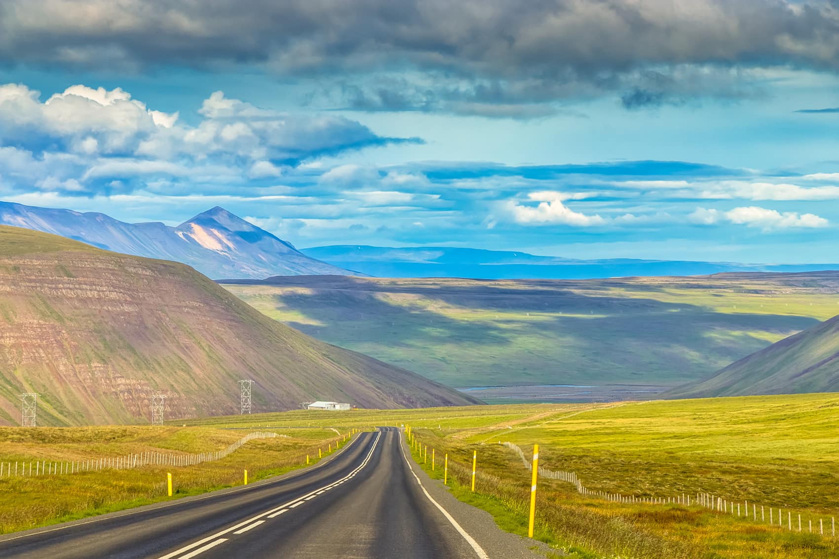 An empty Icelandic road running through green valleys toward distant mountains