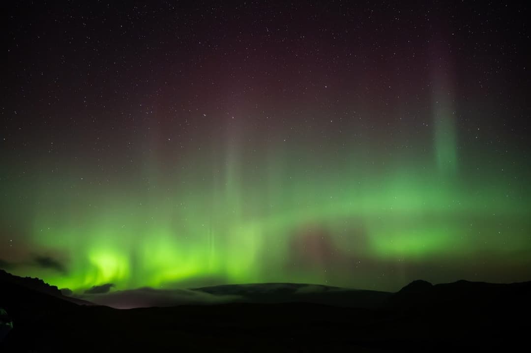 Green and red aurora over dark hills in Iceland