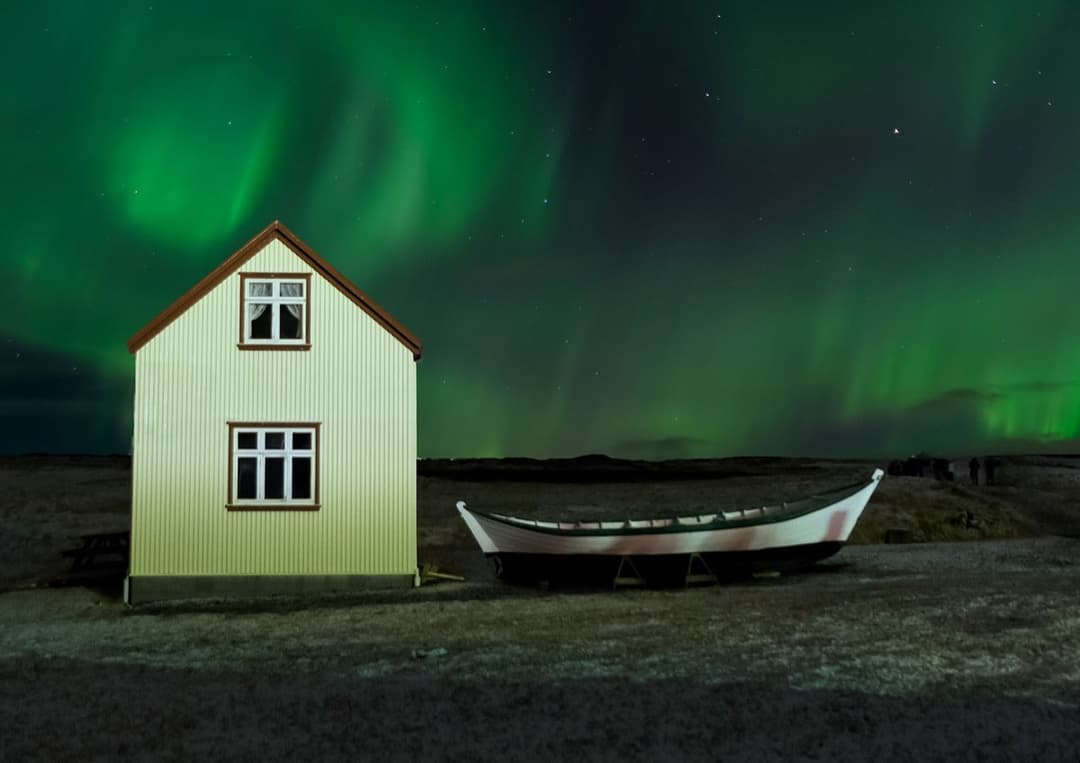 Green aurora over a white Icelandic farmhouse and a beached boat