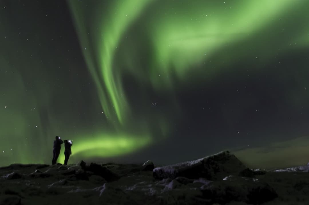 Two people watching the aurora from a rocky ridge